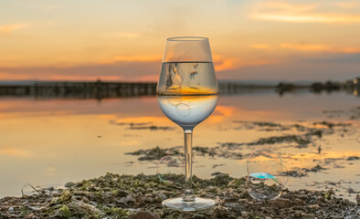Vue d'un verre à vin en cristal avec un coucher de soleil sur les parcs à moules d'un étang de...