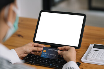 Close up of woman hands holding credit card and using laptop, tablet blank white screen. Online shopping concept.