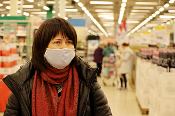 Woman in warm clothes and medical mask choosing products in a supermarket. Concept of safety during shopping at coronavirus pandemic