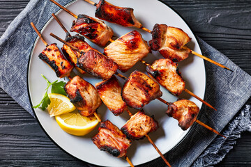 Juicy grilled pork kebabs on a plate on a black wooden table, flat lay, free space