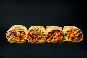 Four juicy shawarma rolls with meat and vegetables on a dark background. Close-up