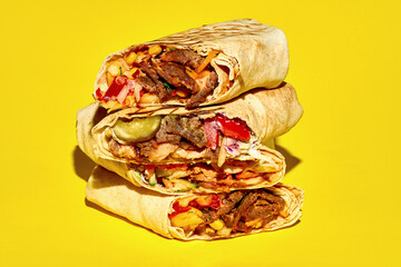 A stack of different shawarma with meat, vegetables and falafel on a yellow background. Close-up, selective focus