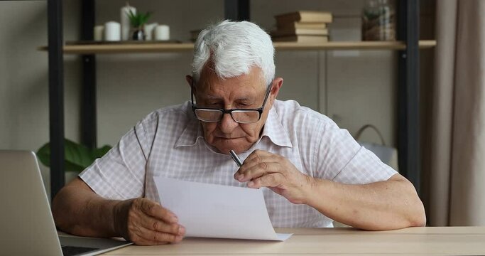 Focused retired man engaged in work on paper document make will read insurance contract consider on agreement terms conditions before signing. Aged male in glasses think on financial report from bank