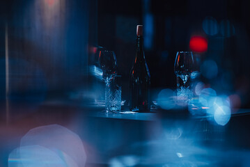 Bottle and glasses in cool artistic light with bokeh and lens flare. Restaurant table setting in an...