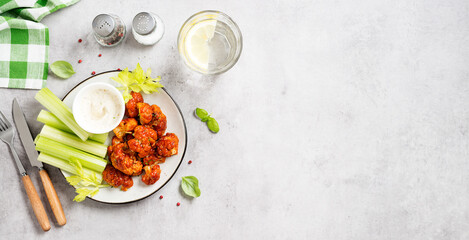 Buffalo style barbecue cauliflower with fresh celery sticks and sauce . Light gray stone background. Top view. Space for text