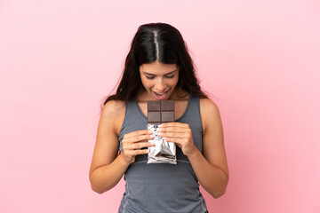 Young caucasian woman isolated on pink background eating a chocolate tablet