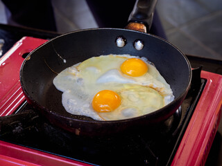 Twin fried egg in pan. Close up top view of the double fried eggs on a frying pan with red picnic gas stove.
