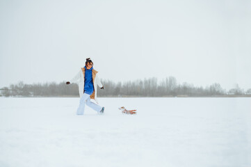 Cheerful female owner runs with a small dog on a snowy field and plays. A walk in the winter with a dog Jack Russell