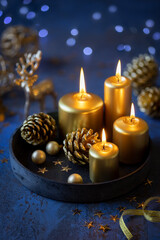 Christmas greeting card with lit golden candles, pine cones festive decorations against dark blue shabby background