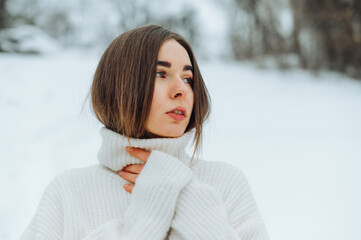 Portrait of a beautiful woman in a white sweater on a snowy street, looking at the camera with a serious face.