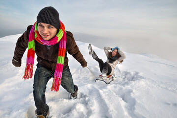 Fototapeta na wymiar Man pulling girl on a sled at snow (concept: Winter fun)