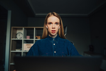 Shocked freelancer woman working at home on laptop and looking at camera with surprised face.