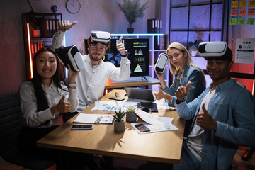 Team of four multiracial IT professionals smiling and looking at camera with thumbs up while...