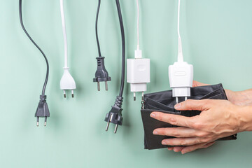 Many power cable cords with Eu plugs hanging over open wallet in woman hands. Electricity cost and...