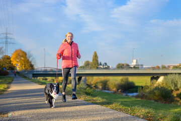 Fit athletic woman running with her Border Collie along footpath