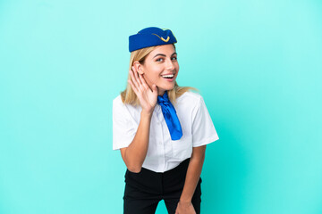 Airplane stewardess Uruguayan woman isolated on blue background listening to something by putting hand on the ear