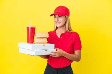 Delivery Uruguayan woman holding fast food isolated on yellow background looking side