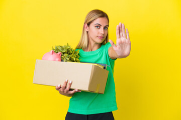 Young Uruguayan girl making a move while picking up a box full of things isolated on yellow...