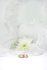 Fototapeta na wymiar Wedding rings and white flower on white tulle background
