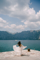 The bride spins on the pier in the Bay of Kotor, her skirt flutters around her 