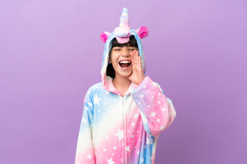 Little kid wearing a unicorn pajama isolated on purple background shouting with mouth wide open
