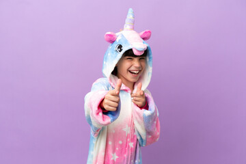 Little kid wearing a unicorn pajama isolated on purple background pointing to the front and smiling