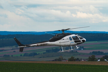 helicopter in flight over an airport with fields and a forest in the background