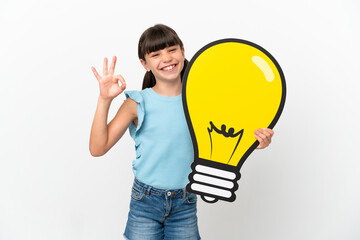 Little caucasian kid isolated on white background holding a bulb icon and doing OK sign