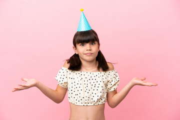 Little caucasian kid with birthday hat isolated on pink background having doubts while raising hands