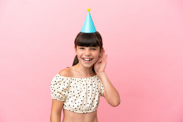 Little caucasian kid with birthday hat isolated on pink background listening to something by...