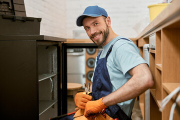 Joyful bearded man repairing fridge in cafe