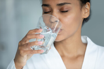 Close up cropped thirsty young african american woman drinking glass of clear pure fresh mineral water, keeping body balance, preventing dehydration, refreshing enjoying daily healthcare habit.