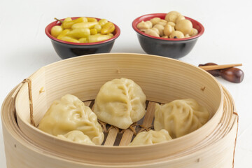 Boiled dumplings, manti or wontons with minced meat in a wooden double boiler with pickled mushrooms and hot peppers on a white table. Homemade food.