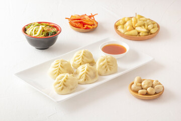 Boiled dumplings, manti or wontons with minced meat in a plate with sauce on a white table along with pickled mushrooms, hot peppers and cabbage salad. Homemade food.