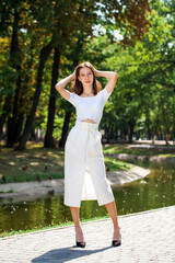 Fototapeta premium Young beautiful brunette girl in a white skirt posing in a summer park