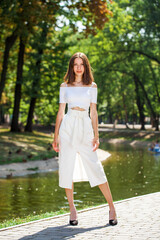 Young beautiful brunette girl in a white skirt posing in a summer park