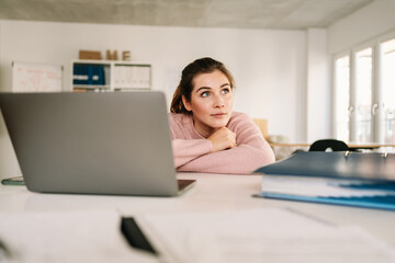 Contemplative young businesswoman leaning forwards on her desk
