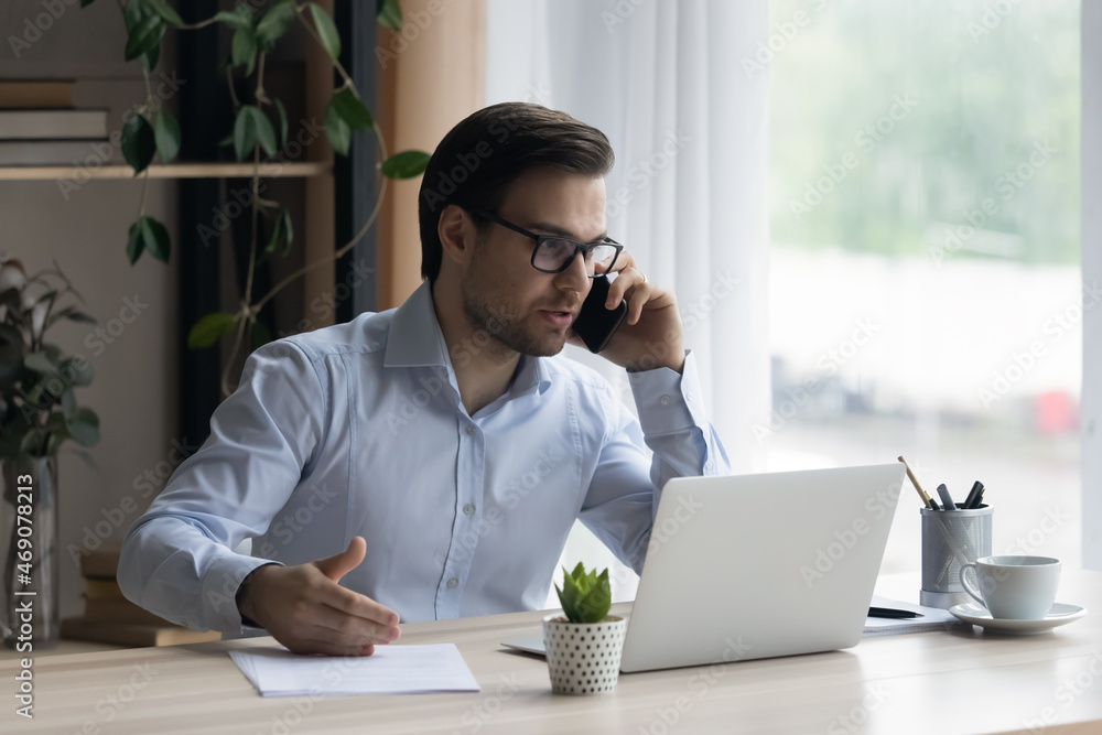 Sticker Focused smiling young businessman in glasses consulting client by phone call, working on computer in modern office. Smart millennial male manager employee multitasking, negotiating project distantly.