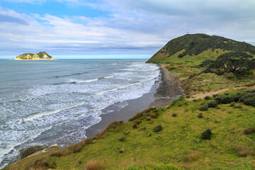 East Cape, the easternmost point on the New Zealand mainland. A lighthouse stands on the hill to the right. Out at sea is Whangaokeno / East Island