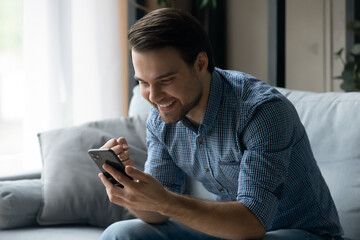 Happy millennial man making yes gesture looking at cellphone screen, celebrating getting online...