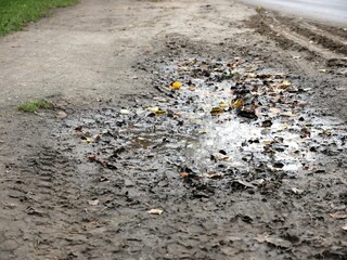 Dirty puddle on the road. Autumn sky reflected in a puddle