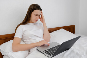 Young serious woman working at home sit in bed with laptop, nervous breakdown, waiting for interview, exam, medical test result, financial issues anxiety, girl depression shocked looking at computer