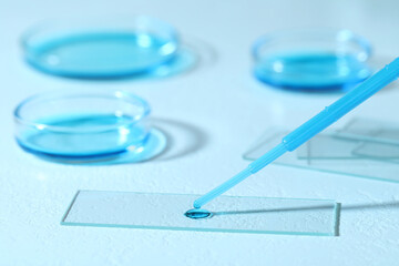 Dripping sample of light blue liquid onto microscope slide on white table