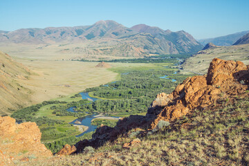 View of a green mountain valley among dry slopes, meanders of the river