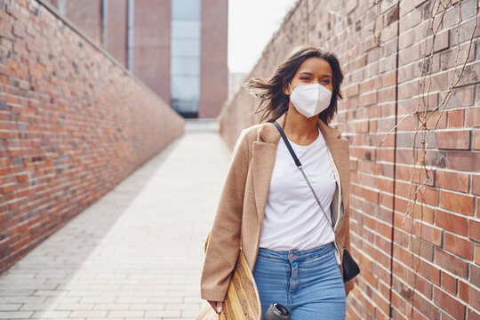 Woman walking through the city wearing protective mask holding skateboard