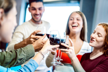 Young multicultural friends drinking and toasting red wine at home party - Happy people having fun together at restaurant winery bar - Dinning life style concept on bright filter - Focus on glasses