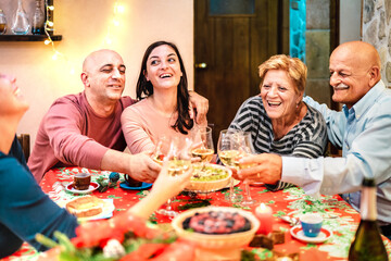 Mixed age group toasting white wine and having fun at winter holiday reunion - Dinner celebration concept with happy adult friends sharing time together at home party - Warm filter with focus on faces