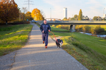 Smiling man running his dog along a footpath at sunset