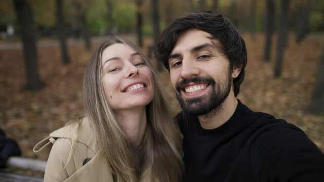 Love couple making selfie on a bench in the park at autumn fall season