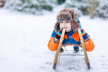 Little kid boy enjoying sleigh ride during snowfall. Happy preschool kid riding on vintage sledge....
